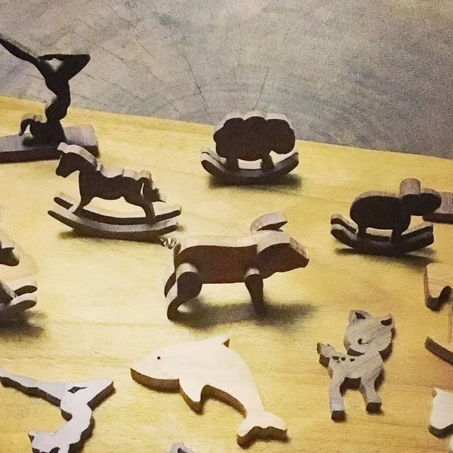 Bichos recortados em madeira sobre uma mesa amarela: cavalo de balanço, ovelha, tatu, gato e golfinho.