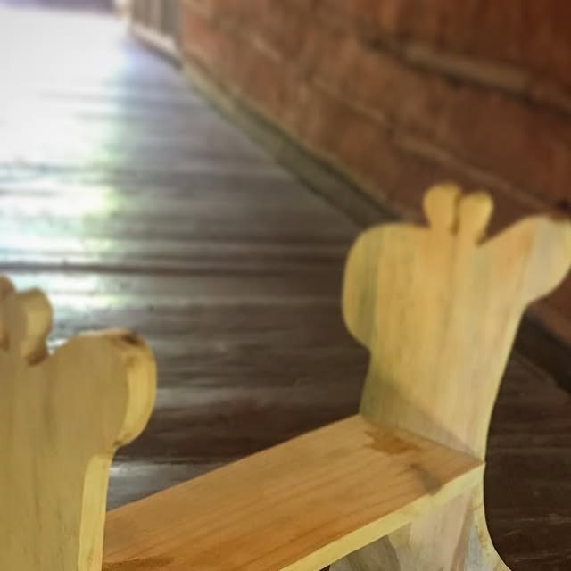 Cadeira infantil em madeira clara, com encosto recortado, sobre um deque.