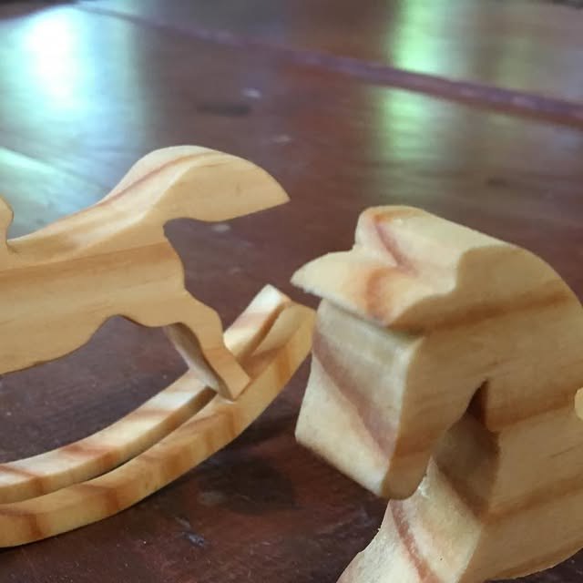 Dois cavalos de balanço pequenos em madeira clara sobre uma mesa.